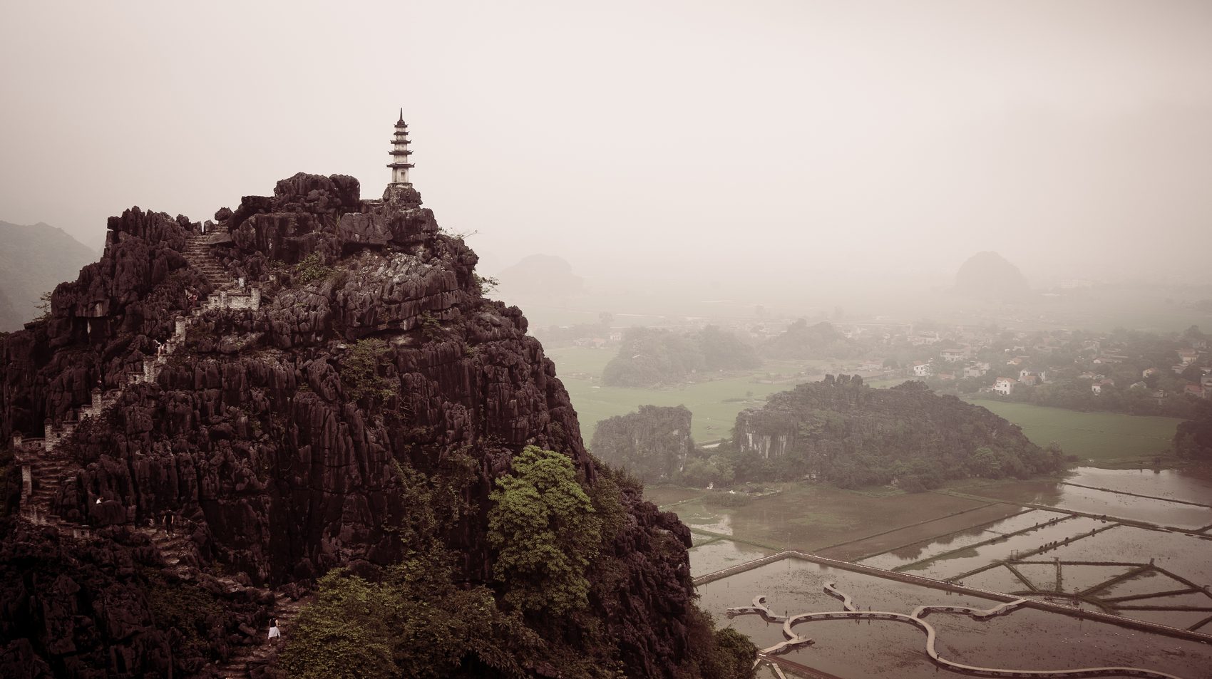 A pagoda on a limestone peak above misty rice fields